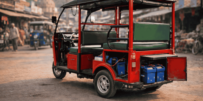 A realistic electric rickshaw parked on a busy market street with its battery compartment visible, showing a clean, quiet vehicle designed for short-distance travel in Indian towns.